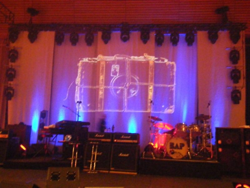 Bühnenaufbau von BAP während der "Radio Pandora"-Tour 2008/09. Im Hintergrund eine große Leinwand mit abstrakten Lichteffekten, umgeben von professioneller Bühnenbeleuchtung. Im Vordergrund sind Musikinstrumente wie Schlagzeug, Keyboards und Verstärker zu sehen.