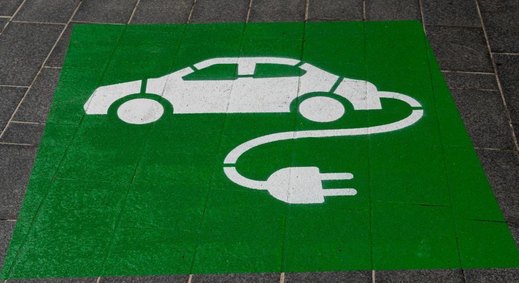 Symbol für E-Auto-Ladestation: weißes Auto mit Ladekabel auf grünem Untergrund