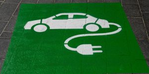 Symbol für E-Auto-Ladestation: weißes Auto mit Ladekabel auf grünem Untergrund