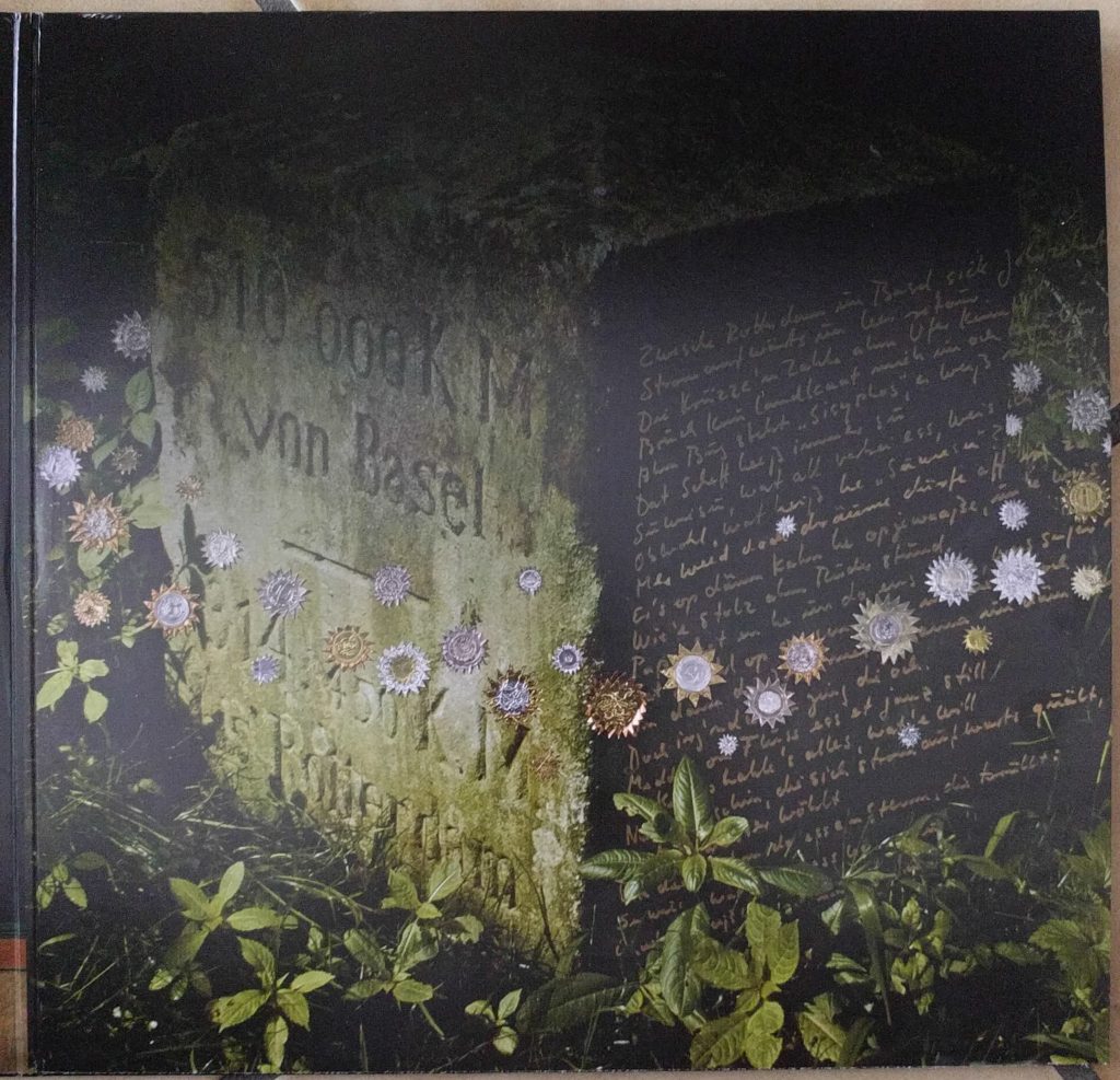 Innenansicht eines Vinyl-Gatefold-Albums: Zu sehen eist ein bearbeiteter Steinquader mit der eingarvierten Schrift "510 KM von Basel - 314 KM bis Rotterdam" und dem handschriftlich verfassten Text des Liedes "Suwiesu" auf der rechten Seite. Drumherum sind Blätter und kleine Sternenaufkleber in verschiedenen Farben zu sehen.
