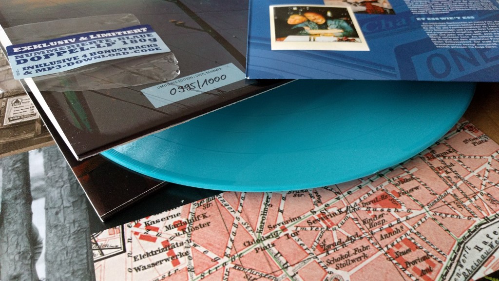 Eine limitierte Vinyl-Schallplatte mit der Aufschrift "Exklusiv & Limitiert" und der Nummer 0995/1000. Daneben liegt eine blaue Schallplatte mit einer Stadtkarte als Design. Im Hintergrund sind weitere Schallplattenhüllen zu sehen.