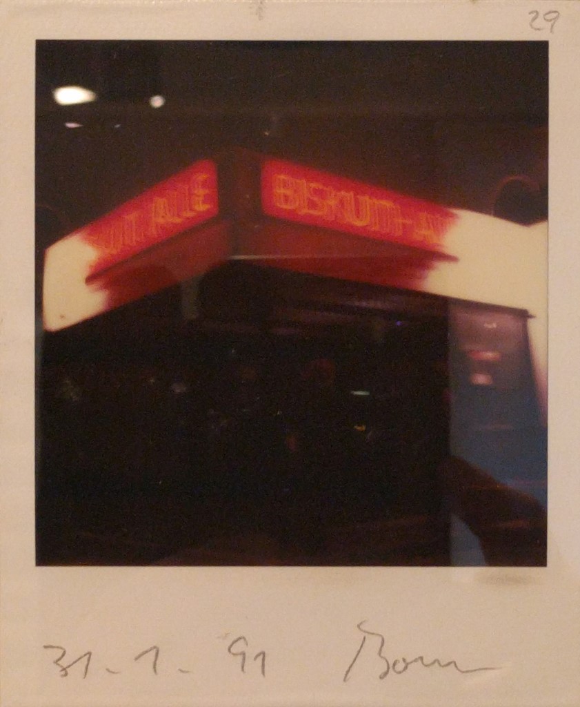 Ein leicht unscharfes Polaroid-Foto mit der Aufschrift "BISKUITHALLE" in orangen Leuchtbuchstaben auf rotem Hintergrund. Unten steht handschriftlich "31.1.91 Bonn".