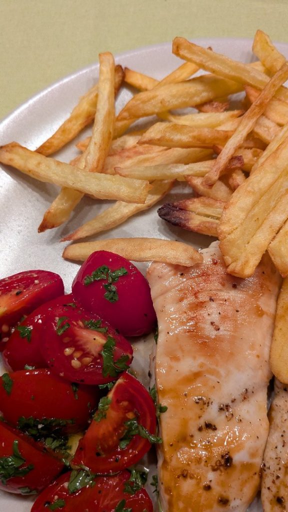Ein Teller mit gebratenem Hähnchenbrustschnitzel, Pommes frites und einem Tomatensalat, garniert mit frischer Petersilie.