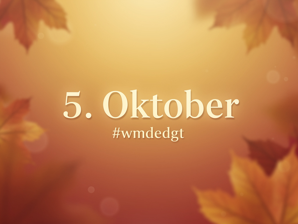 Herbstlicher Hintergrund in warmen Orange-, Gelb- und Brauntönen mit unscharfen Ahornblättern. In der Bildmitte steht der Text "5. Oktober" in großer, weißer Schrift, darunter der Hashtag "#wmdedgt".