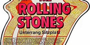 Ticket mit dem Rolling-Stones-Zungen-Logo: ein großer roter Mund mit herausgestreckter Zunge. Im Inneren des Mundes steht in roten Buchstaben „THE ROLLING STONES“. Darunter ist in schwarzer Schrift „Unterrang Sitzplatz“ aufgedruckt, ergänzt um Angaben zum Vorverkauf und weitere kleingedruckte Details. Das Ticket hat einen goldenen Rand, die Farbigkeit ist Rot, Gold und Schwarz.