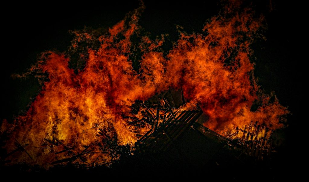 Ein großes Feuer flackert in der Dunkelheit. Orange, gelbe und tiefrote Flammen leuchten vor dem fast schwarzen Hintergrund.