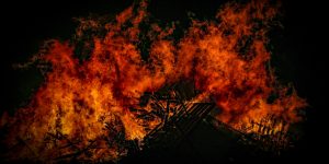 Ein großes Feuer flackert in der Dunkelheit. Orange, gelbe und tiefrote Flammen leuchten vor dem fast schwarzen Hintergrund.